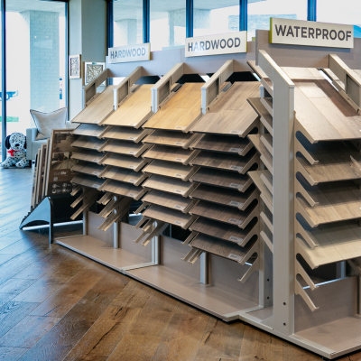Display racks showcasing various hardwood and waterproof flooring samples in different wood tones and textures.